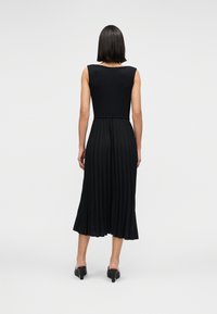 Μαύρο πλισέ φόρεμα με εφαρμοστό μπούστο και φουσκωτή φούστα· κατασκευασμένο από απαλό ύφασμα, με λαιμόκοψη σε σχήμα scoop και αμάνικη σχεδίαση, με ελάχιστες λεπτομέρειες.