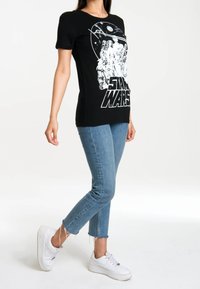 Černé tričko s bílým grafickým designem "Star Wars", krátké rukávy a kulatý výstřih, doplněné o modré oprané džíny a bílé tenisky.