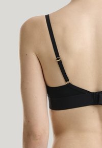 Reggiseno nero con spalline regolabili, chiusura a gancio e tessuto liscio dal design minimalista. Piccole decorazioni in metallo dorato.