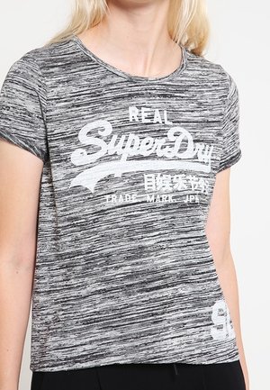 Kobieta w szaro-czarnej melanżowej koszulce SuperDry z krótkim rękawem i białym logo na przodzie.