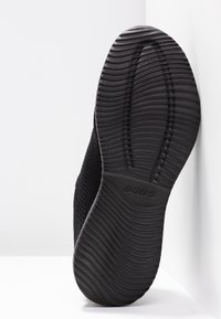Černá sportovní bota s texturovanou gumovou podrážkou, s flexibilním pleteným svrškem a logem "BOBS" vytlačeným v oblasti paty.