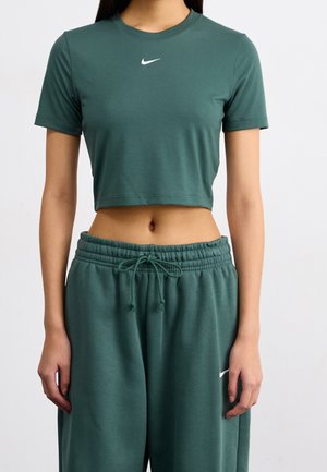 Personne portant un t-shirt court Nike vert foncé et un pantalon de survêtement assorti avec cordon de serrage et logo Nike sur la cuisse gauche.