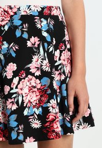 Falda floral con fondo negro y flores rojas, rosas y azules. Está hecha de un tejido texturizado con detalles de diseño plisado.