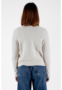 Maglione beige con texture, colletto rotondo e maniche lunghe, abbinato a jeans in denim larghi. Il maglione presenta orli e polsini a costine.