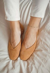 Bailarinas de ante color canela con un escote en forma de V puntiagudo, textura suave y un diseño liso y limpio. Se llevan con pantalones blancos recortados.