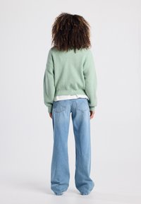 Green ribbed knit sweater with dropped shoulders, paired with light blue wide-leg jeans featuring back pockets and stitching accents.