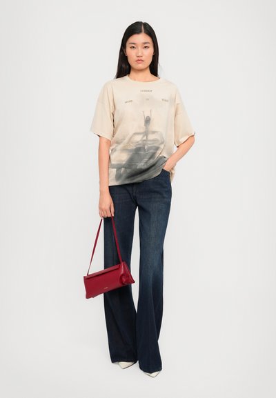 Camiseta oversize beige con estampado gráfico, combinada con jeans de pierna ancha azul oscuro. Lleva un bolso de cuero rojo. Zapatos de punta blanca.