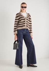 Ριγέ καφέ και μπεζ ζακέτα, κουμπωμένη, συνδυασμένη με σκούρες μπλε φαρδιές τζιν παντελόνες. Η μαύρη τσάντα με καρφιά και τα μυτερά μαύρα παπούτσια ολοκληρώνουν την εμφάνιση.