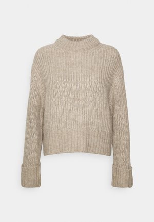 Pull beige en maille épaisse avec col montant côtelé, manches longues repliées aux poignets et un ourlet légèrement raccourci.