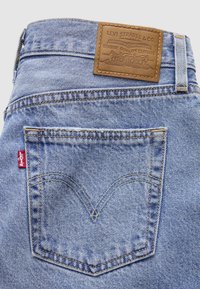 Jean en denim bleu clair avec poche arrière, étiquette rouge Levi's et écusson en cuir marron Levi Strauss & Co. sur la ceinture.