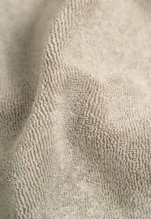 Beige plush fabric with a textured, raised pattern. Soft, absorbent material, draping slightly, showing a smooth surface and subtle sheen.