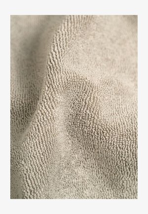 Beiger Plüschstoff mit einem strukturierten, erhabenen Muster. Weiches, saugfähiges Material, das leicht fällt und eine glatte Oberfläche sowie einen subtilen Glanz zeigt.