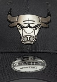 Μαύρο ρυθμιζόμενο καπέλο με μεταλλικό λογότυπο ταύρου στο μπροστινό μέρος και στρογγυλή ετικέτα New Era 9FORTY στην κάτω πλευρά της γρίλιας.
