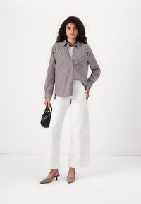 Striped button-up shirt in beige and navy, paired with wide white trousers. Black handbag and light grey slingback heels complete the look.