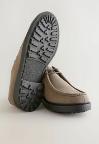 Pantofi din suede maro cu vârful rotund, având o talpă din cauciuc negru cu modele texturate pentru aderență și șireturi maro.