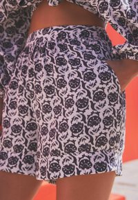 Bermudas blancas con un estampado floral negro, con una cintura elástica y bolsillos laterales, que ofrecen un ajuste relajado y un tejido ligero.