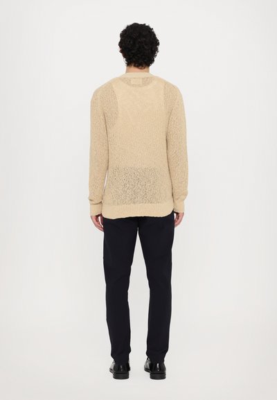 Beige strikket genser med et teksturert mønster, lange ermer og rund hals, kombinert med mørke, slim-fit bukser.