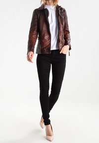Giacca di pelle marrone con una finitura leggermente testurizzata, zip stilizzata e silhouette aderente. Abbinata a jeans skinny neri e tacchi nudi.