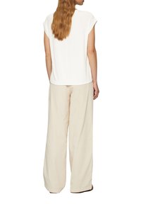 Witte korte mouwen top met een ronde hals, gecombineerd met lichtbeige wijde broek. De stof lijkt zacht; de broek heeft een relaxte fit.