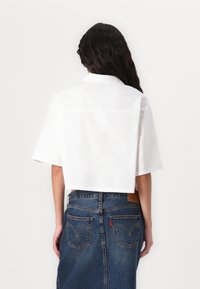 Camisa branca de botão, cortada, com mangas curtas, feita de algodão tecido. Saia de ganga com bolsos traseiros e um logo em couro na cintura.