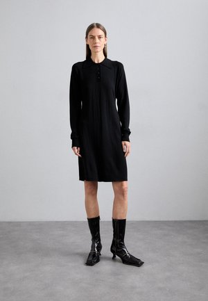 Black long-sleeve dress with a collar and button placket, made from soft fabric. Paired with glossy black knee-high boots.