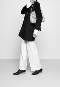 Black oversized coat, white turtleneck, wide white trousers. Black pointed-toe shoes with clear heel. Light gray handbag with structured design.