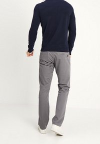 Pantaloni chino grigi con una texture liscia, caratterizzati da una vestibilità standard e dettagli sulla tasca posteriore, abbinati a una camicia a maniche lunghe di colore scuro.