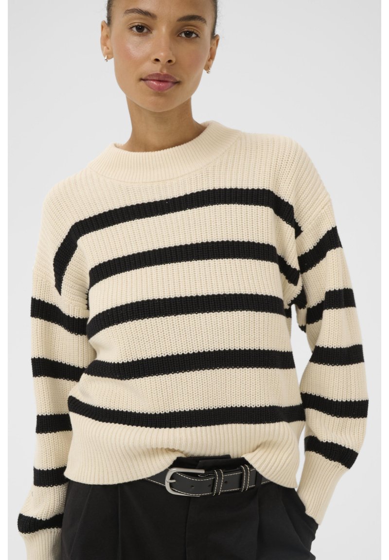 Knit sweater in cream with black horizontal stripes. Features a crew neckline and ribbed cuffs. Worn over black pants with a belt.