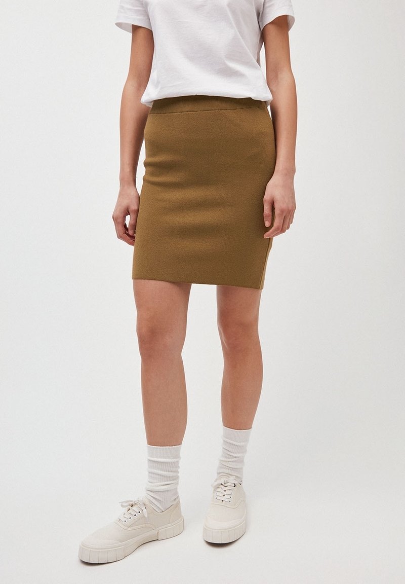 Gonna mini a maglia verde oliva con una cintura elastica, abbinata a una t-shirt bianca, sneakers bianche e calzini a coste.