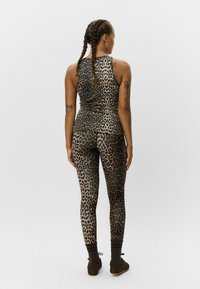 Lietus raksta sporta apģērbu komplekts, kas sastāv no pieguļoša bezpiedurkņu topa un pilna garuma legingiem, izgatavots no stiepļu auduma ar gludu tekstūru.