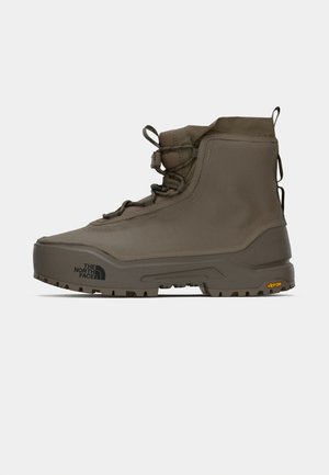 Botte de randonnée montante marron avec semelle épaisse, devant à lacets, languettes de tirage, et logos "The North Face" et "Vibram" sur la semelle et le côté.