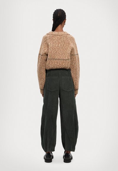 Stribet, brun strikket sweater med bred krave, parret med mørkegrønne kordfløjl bredbenede bukser. Bagfra ses to baglommer.