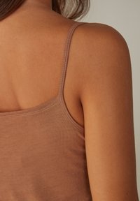 Top de algodón marrón sin mangas con tirantes finos, diseño ajustado, textura suave y detalles de costura sutiles, que muestra la zona de los hombros y la parte superior de la espalda.