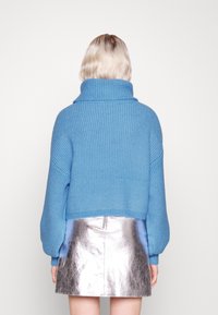 Maglione a coste azzurro chiaro con colletto alto e maniche oversize, abbinato a una mini gonna argentata lucida.