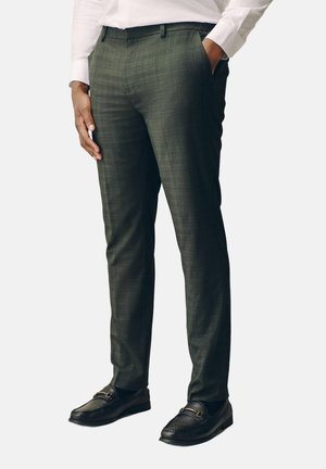 Mann trägt dunkelgraue Slim-Fit-Anzughose mit dezentem Karomuster und schwarze Loafers, Hand in der Hosentasche und weißes Hemd.