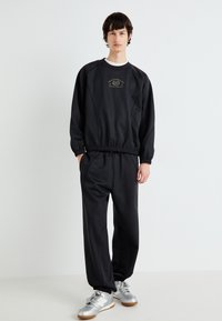Hanorac negru și pantaloni asortați din material moale. Include talie elastică și manșete, margine ribbed și detaliu cu logo imprimat.