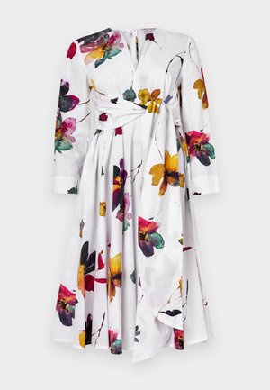 Witte jurk met lange mouwen, bloemenprint in paars, geel en rood. Kenmerkt zich door een geknoopte taille en een uitlopende rok.