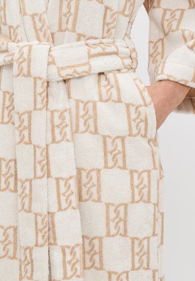 Valge rüü tekstuuriga pinnaga, millel on heledat pruuni geomeetriline muster. Sisaldab vöörihma ja taskuid mõlemal küljel.