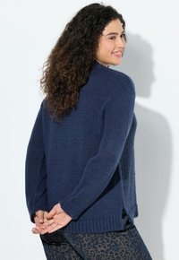 Marineblauer Strickpullover mit langen Ärmeln, geripptem Saum, seitlichen Schlitzen und strukturiertem Stoff, kombiniert mit bedruckten Hosen.