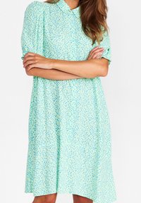 Jasnozielona sukienka z kołnierzykiem, krótkimi bufkami i luźnym krojem, z rozproszonym niebieskim wzorem na całej powierzchni.