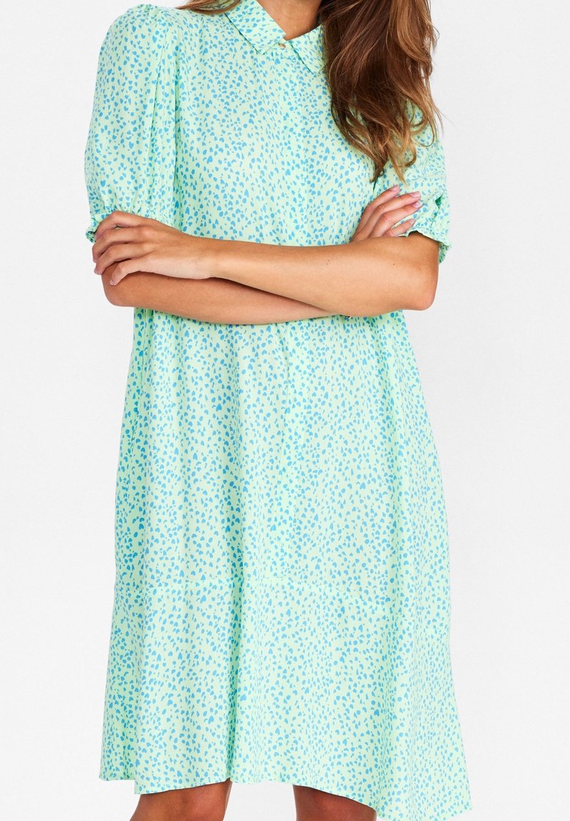 Jasnozielona sukienka z kołnierzykiem, krótkimi bufkami i luźnym krojem, z rozproszonym niebieskim wzorem na całej powierzchni.