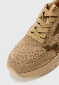 Beige Sneaker mit strukturiertem Obermaterial aus flauschigem Material und Wildlederakzenten, goldenen metallischen Details und klassischem Schnürdesign.