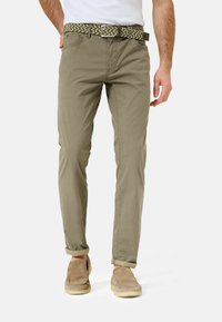 Khaki broek met een fitted snit, voorzien van een geweven riem met textuur in groen en beige tinten. Opgerolde mouwen en lichtbeige instapschoenen.