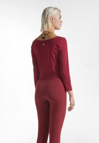 Bordeauxrode top met lange mouwen, een ronde hals, een aansluitende pasvorm en een gladde textuur, gecombineerd met bijpassende aansluitende broek. Klein logodetail op de achterkant.