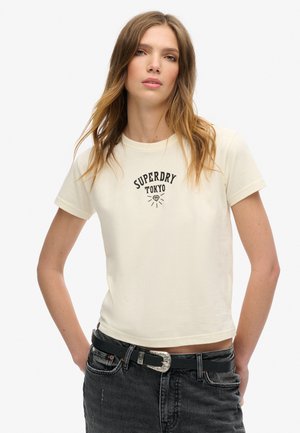 Cremfarbener Kurzarm-T-Shirt mit "SUPERDRY TOKYO"-Grafik in Schwarz. Baumwollmaterial, taillierte Passform, runder Ausschnitt und cropped Länge.