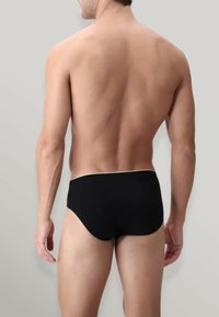 Slip da nuoto neri con un elastico bianco in vita, realizzati in tessuto elasticizzato. Presentano una vestibilità a vita bassa e una superficie liscia, mostrando la vista posteriore.