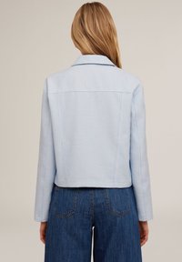 Giacca cropped azzurro chiaro in tessuto testurizzato, colletto a revers e maniche lunghe, abbinata a pantaloni in denim a vita alta.