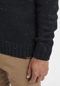 Mörkblå, stickad tröja med färgglada prickar, ribbade ärmslut och nederkant. Har en liten etikett på den nedre sidan. Mjuk och texturerad tyg.