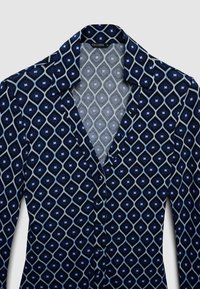 Chemise bleu marine boutonnée avec un motif géométrique de losanges dans différentes nuances de bleu, dotée d'un col classique et d'une texture de tissu lisse.