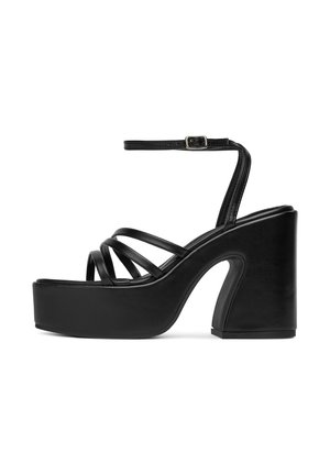 Sandalele platform negre au un toc masiv și mai multe curele subțiri. Sunt construite dintr-un material sintetic neted și au o curea la gleznă.